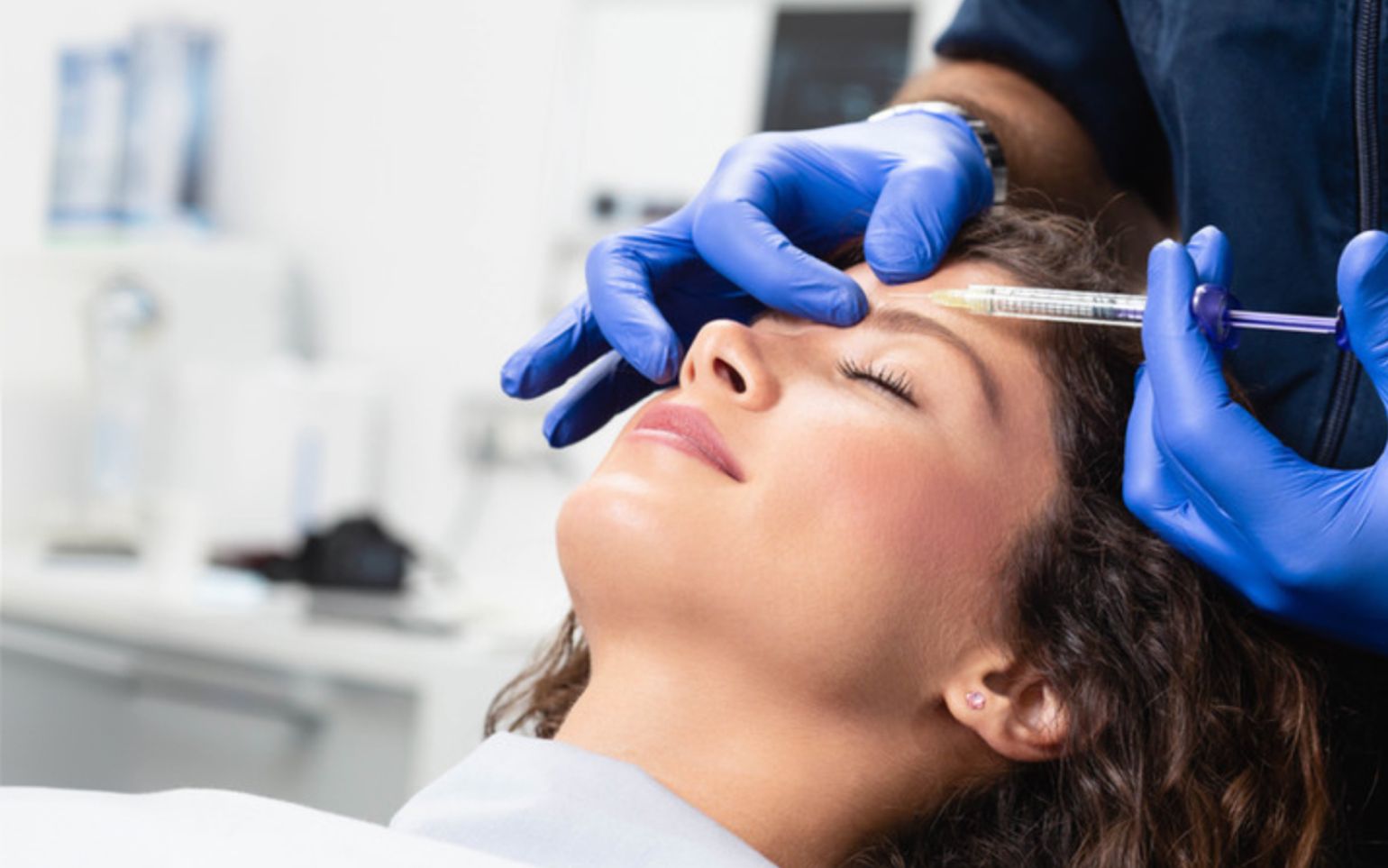 Provider in blue gloves giving a Botox injection to a client's forehead